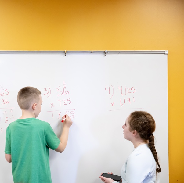 A student and a child solving math problems on the board
