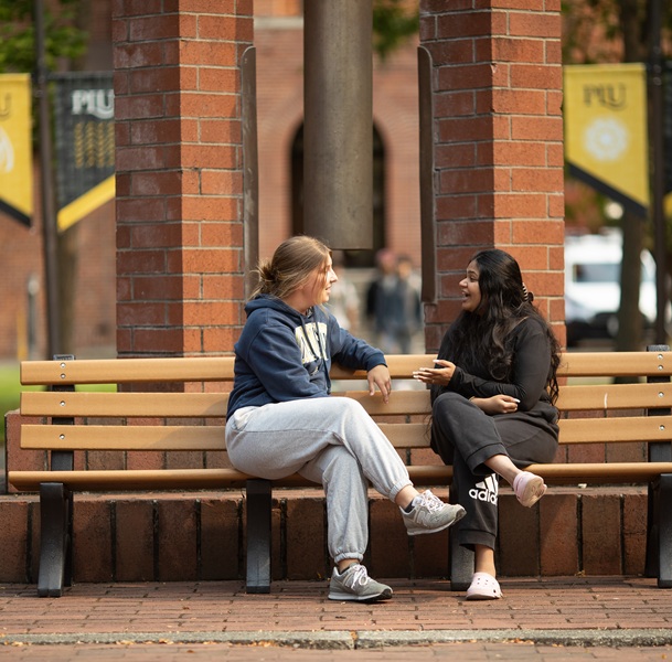 Students chat on a bench with the Centennial Bell behind them