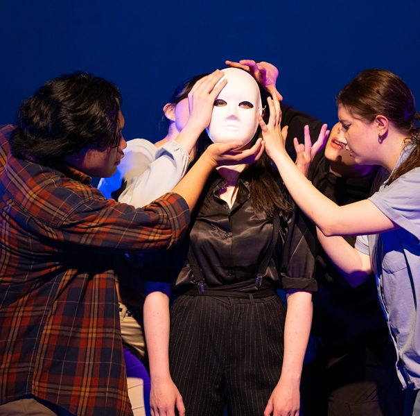 Students performing and centered around a student in a white mask