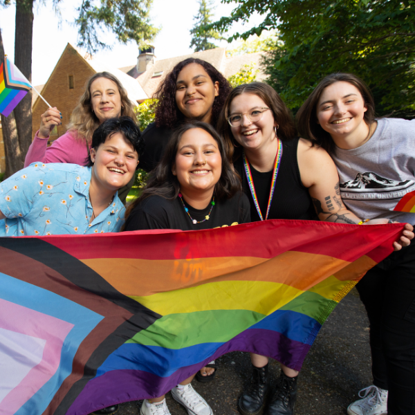 LGBTQ+ students celebrating with flag in a group photo