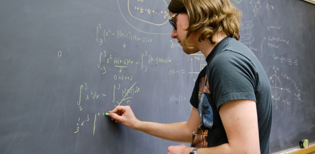 A mathematics student writing equations onto a chalkboard in green chalk.