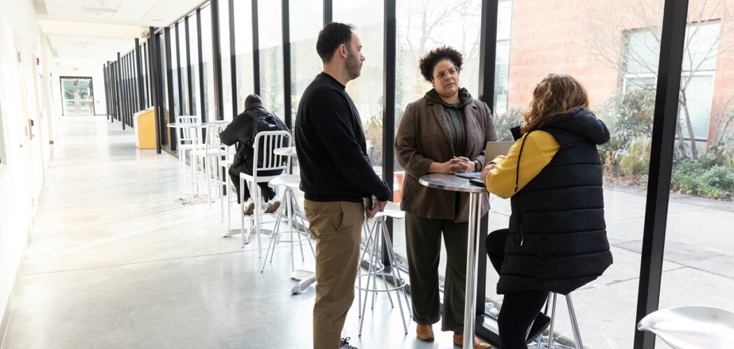 Three EdD students sit/stand and converse at a tall table in the hallway of the Morken Center for Learning & Technology on the PLU campus.