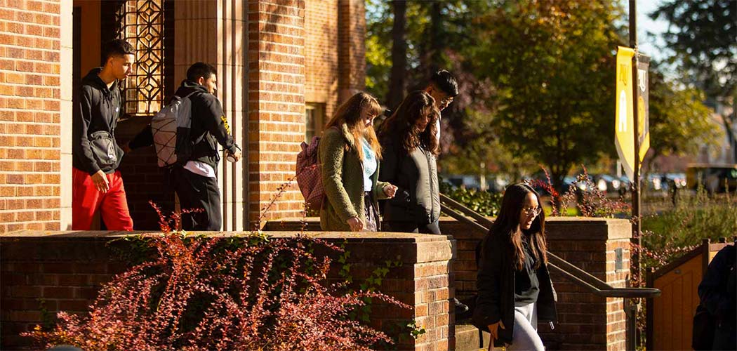 Several students walking out of a building and down some stairs on PLU's campus.