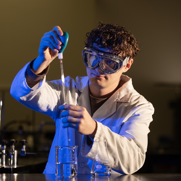 Student in a white coat and glasses doing an experiment in a lab