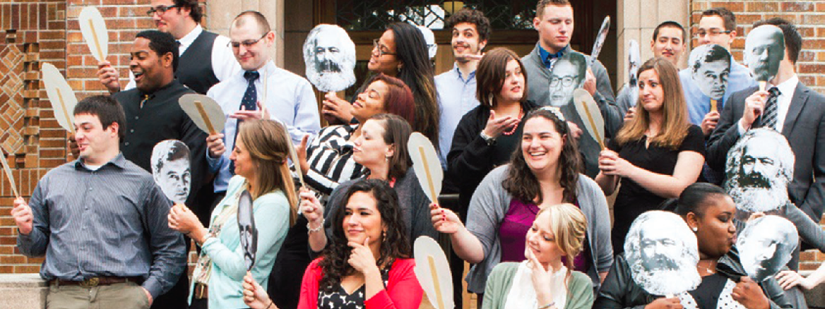 Students and professors holding a face cutout and posing for a picture
