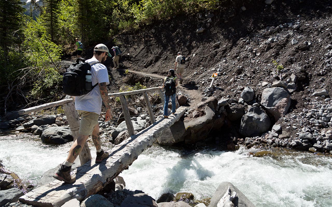 PLU students crossing a creek on a walkway while hiking on Mount Rainier.