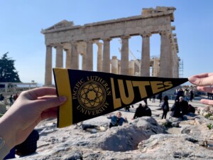 Student holding a Lute Banner in front of the Parthenon in Athens, Greece.