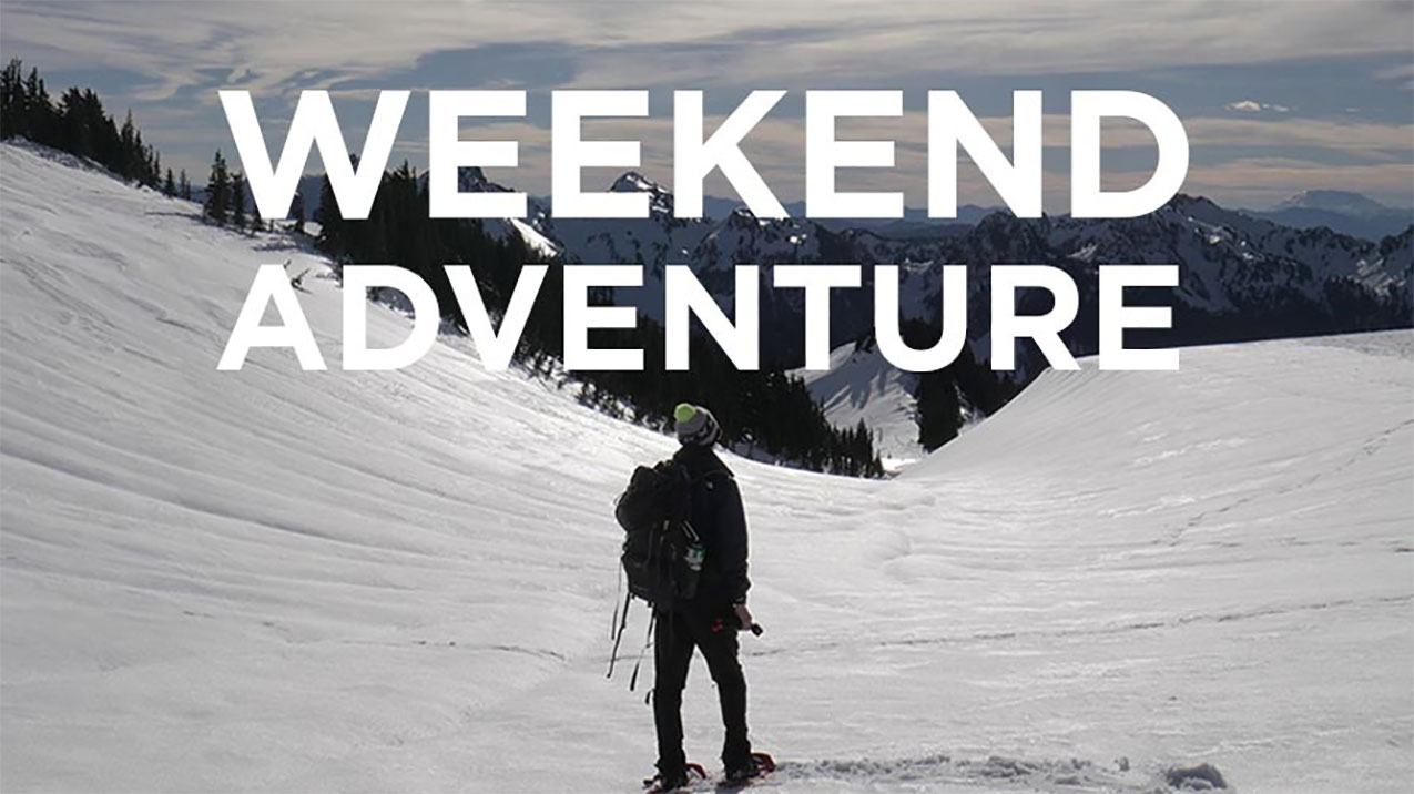 A man is walking in the mountains, on snow with the words "Weekend Adventure" going over the top of it.