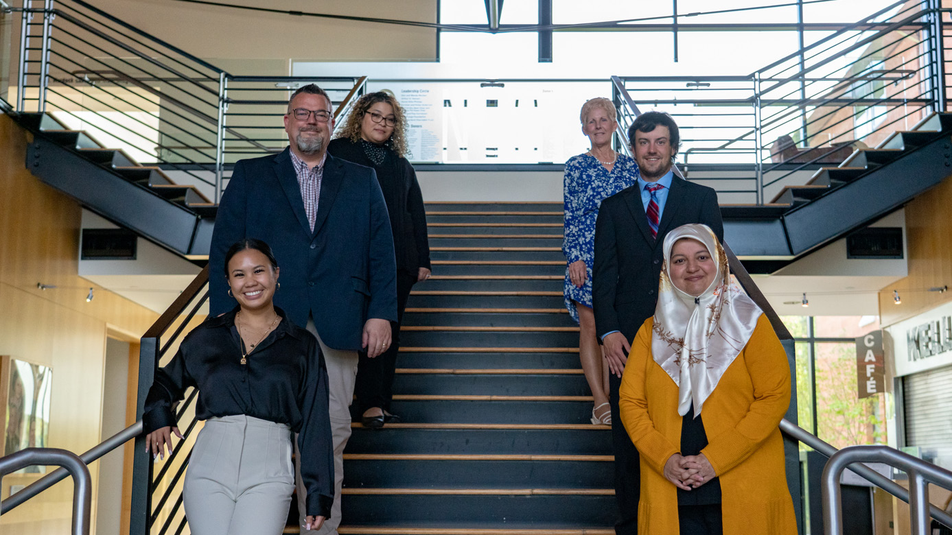 Business professors and students pose on a staircase.