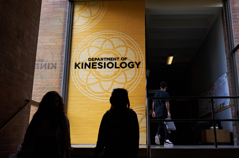 Unidentified students walk y the Department of Kinesiology sign.