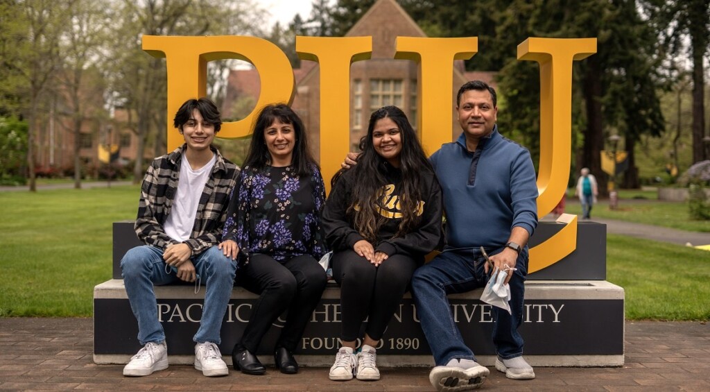 A family of four sits against the PLU monument sign on campus