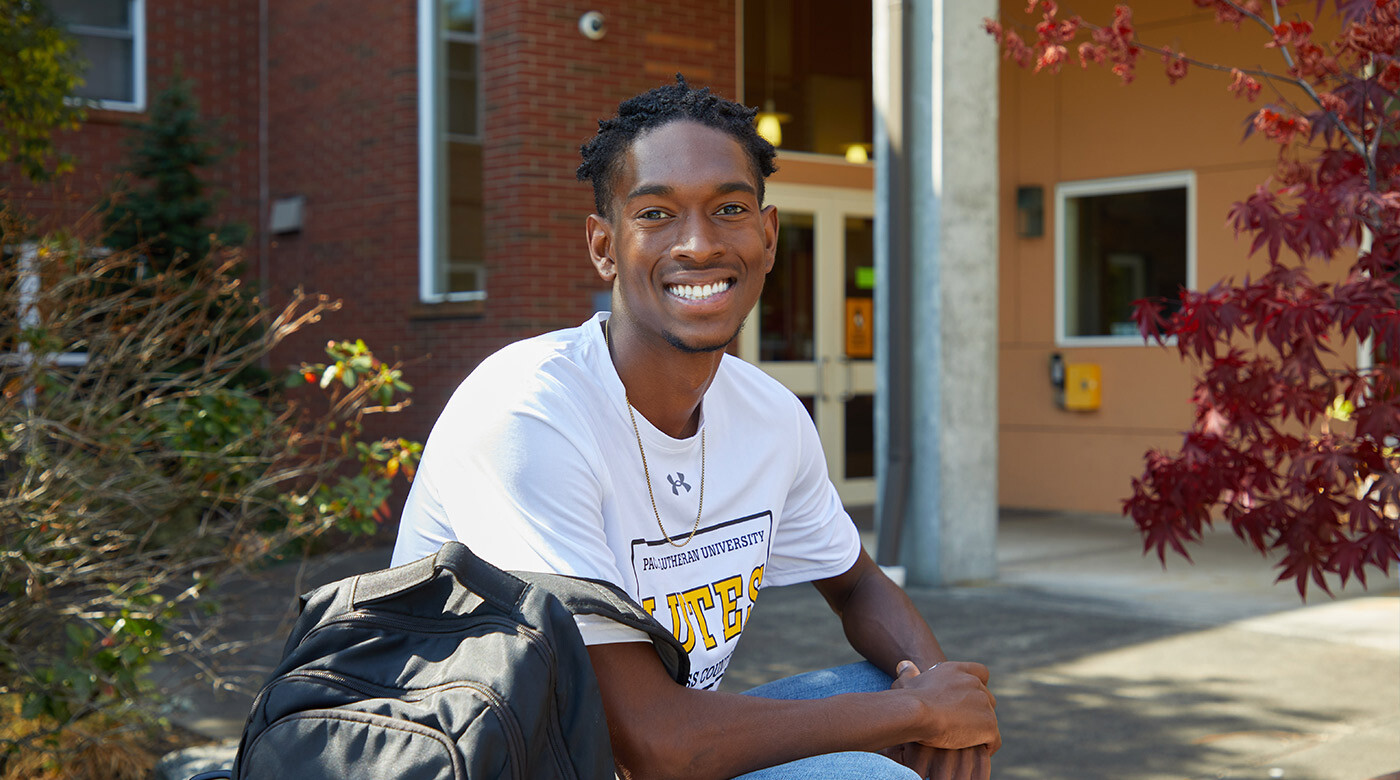 RHA president Hezekiah Goodwin ’22 sits, smiling outside south hall holding his backpack on a sunny fall day