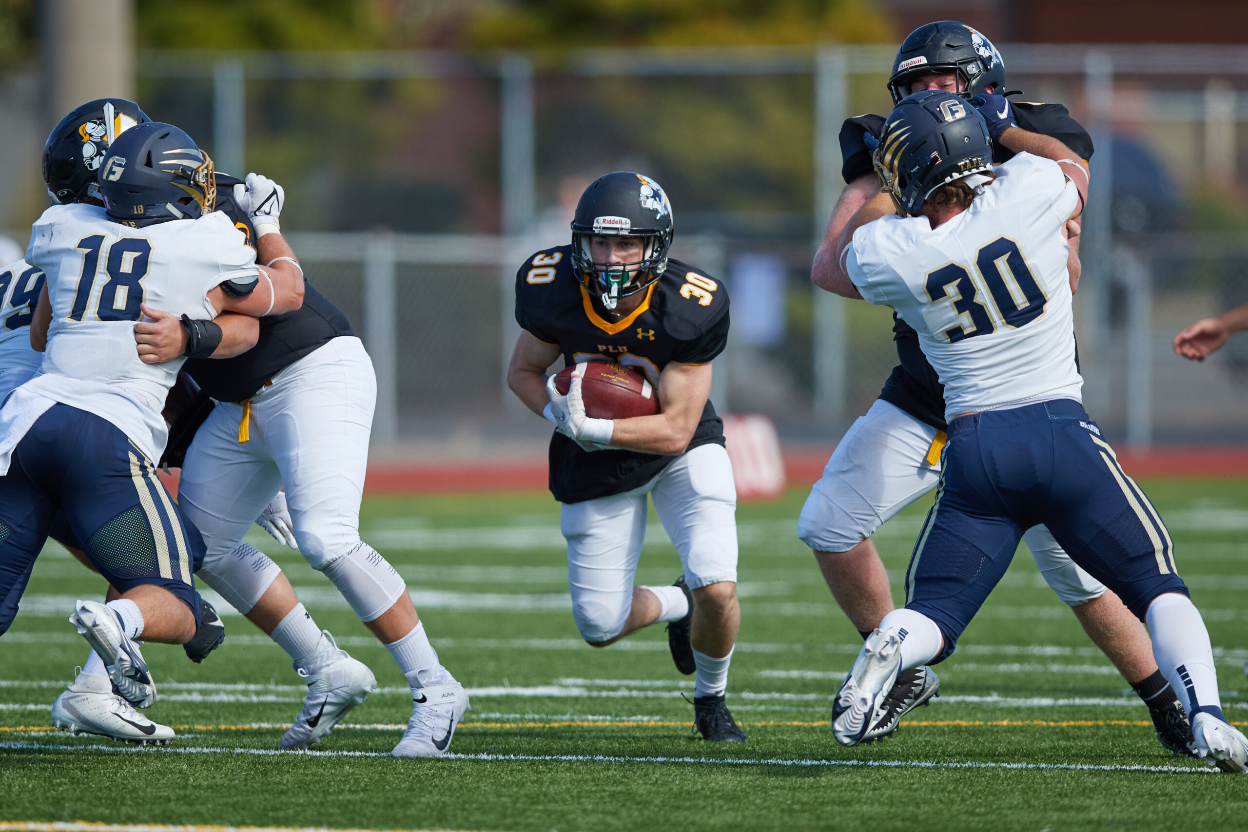 PLU football player runs between two players from George Fox while holding football.