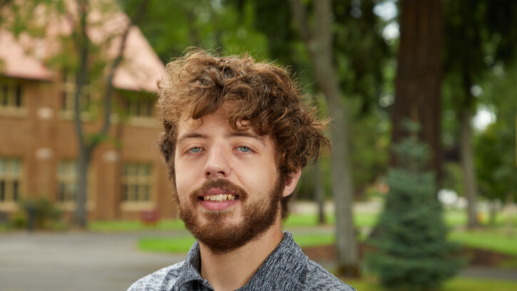 Ian Lindhartsen is seen standing on the PLU campus, looking at the camera wearing a black and white shirt.