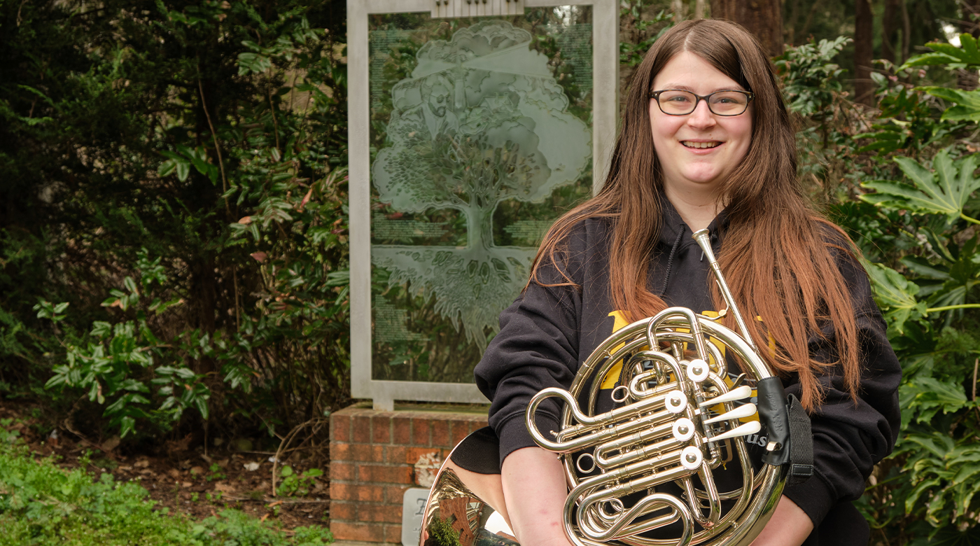 Kaila Harris stands in front of a statue holding a french horn.