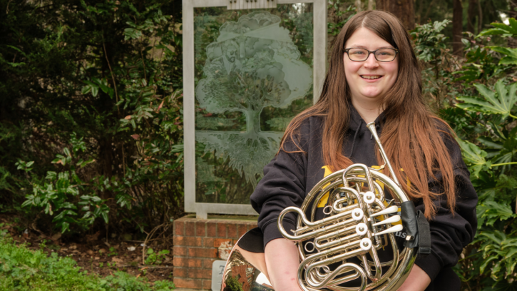 Kaila Harris stands in front of a statue holding a french horn.