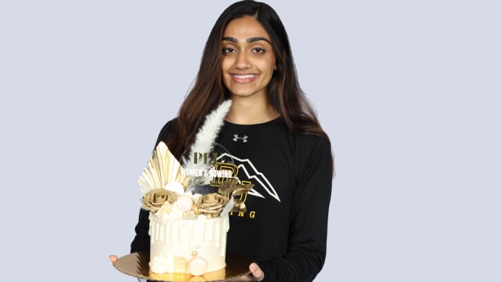 Jasneet Sandhu smiles at the camera while holding a white cake with PLU decoration.