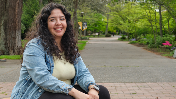Karen Marquez sits in the courtyard at PLU smiling at the camera.