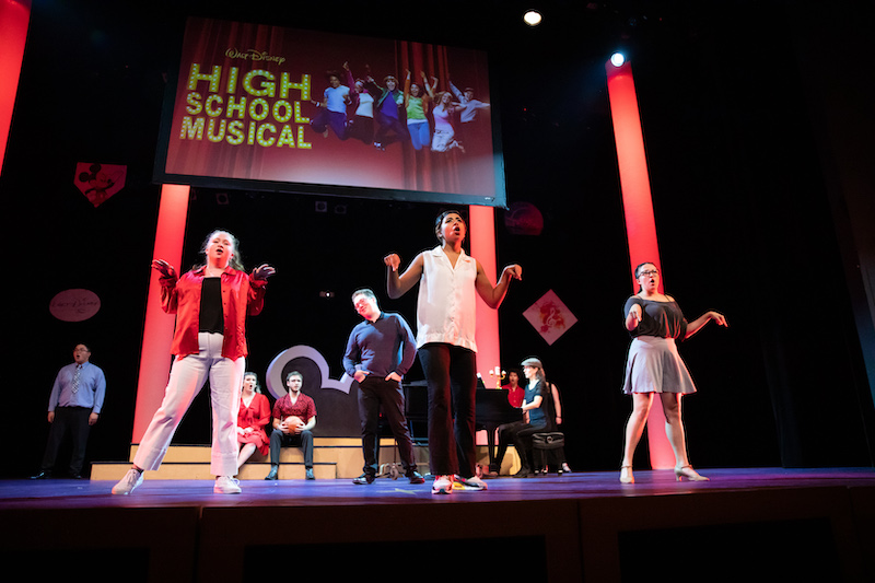 20221007_SB_Wish-Upon-A-Star_268 Eight actors are on a stage in various dance poses. Behind them is a giant screen with the "High School Musical" logo on it.