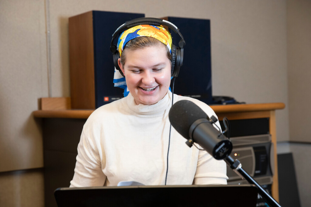 Z Rich sits in front a microphone. She is wearing a yellow headband and cream sweater.