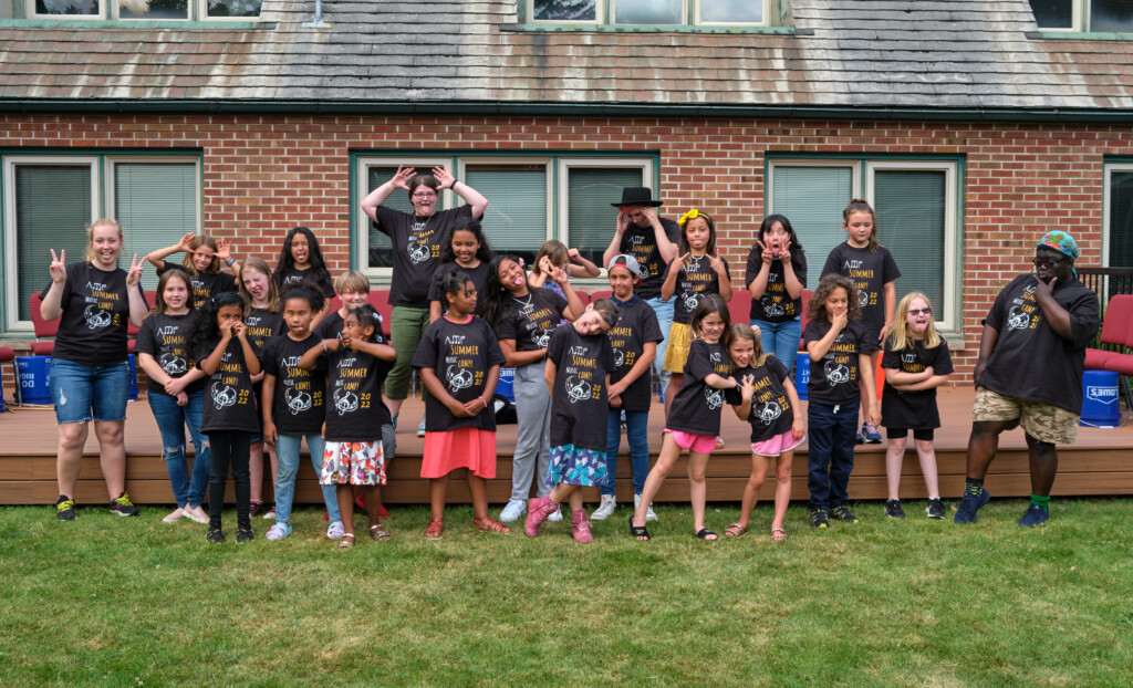 summer-music-camp-7-8-22-169 Children and three college students pose for a silly picture outside of a church.