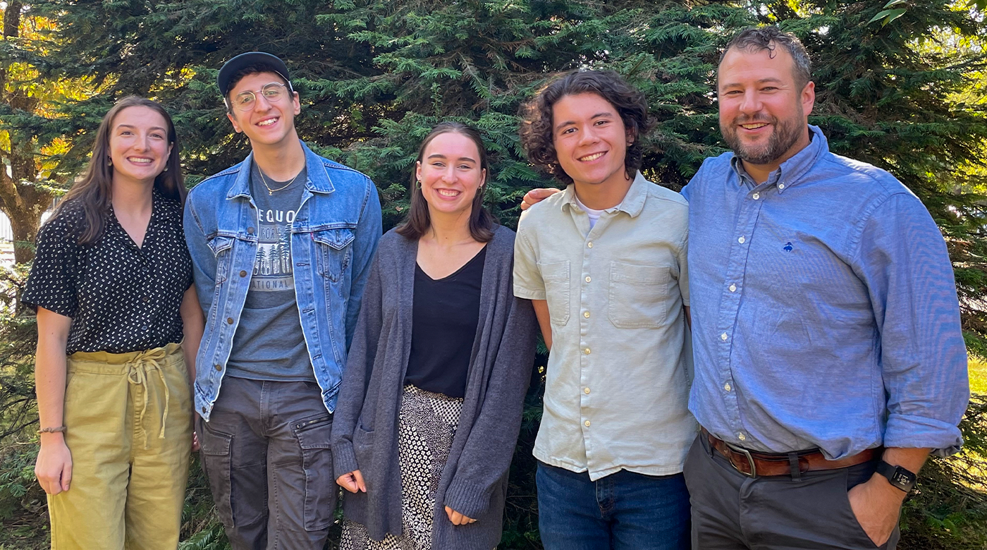 Five individuals stand together in front of a tree.