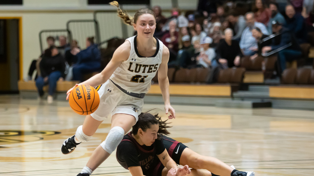Sydney Reisner runs with a basketball during a game at PLU. An opposing player is on the ground beside her.