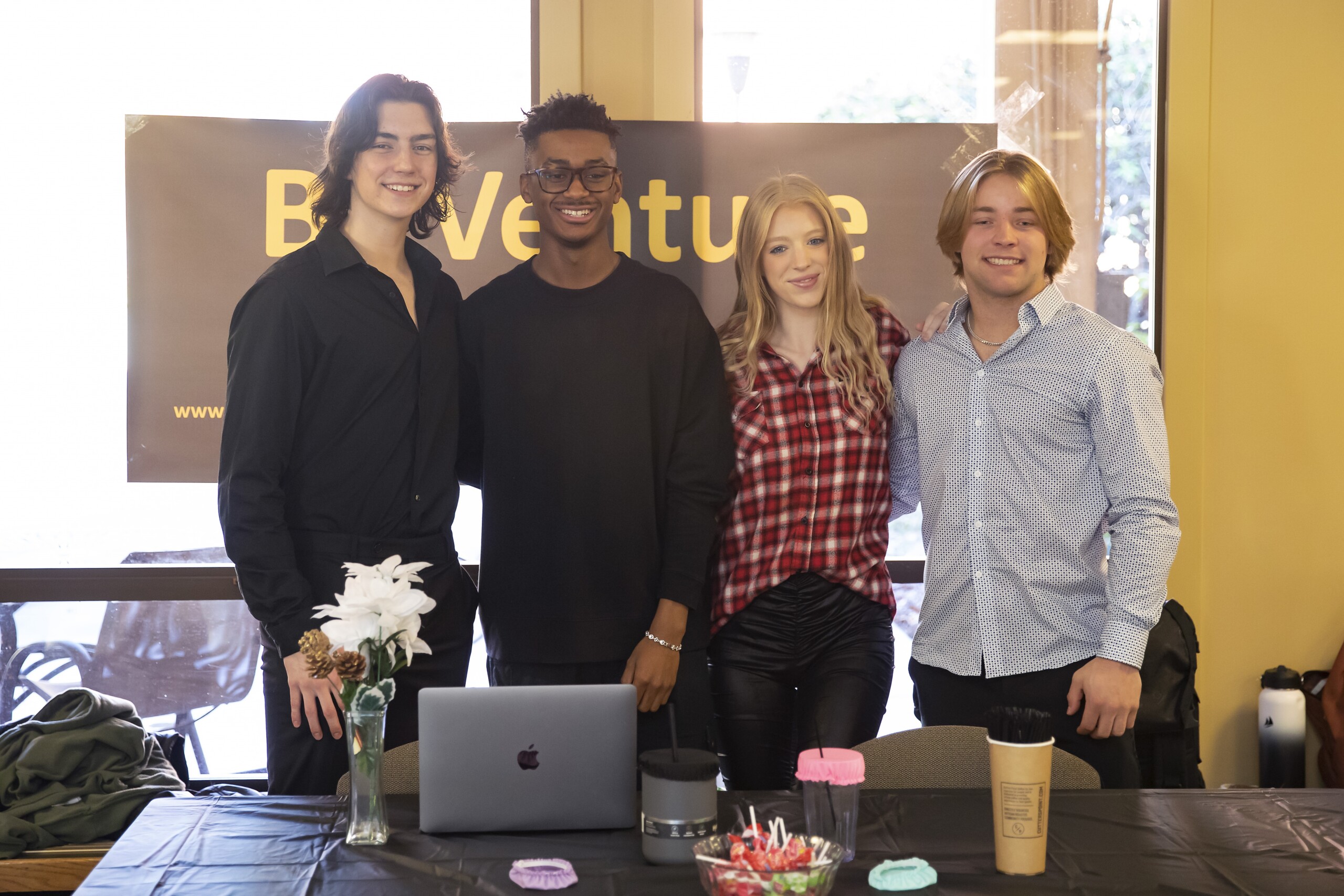 Four business students stand and smile together behind a table during PLU's Biz Venture Day