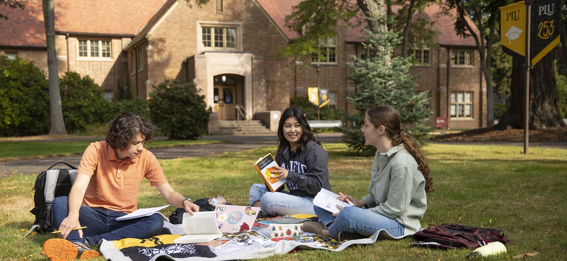 Students study on the grass outside Xavier building on a sunny day on campus