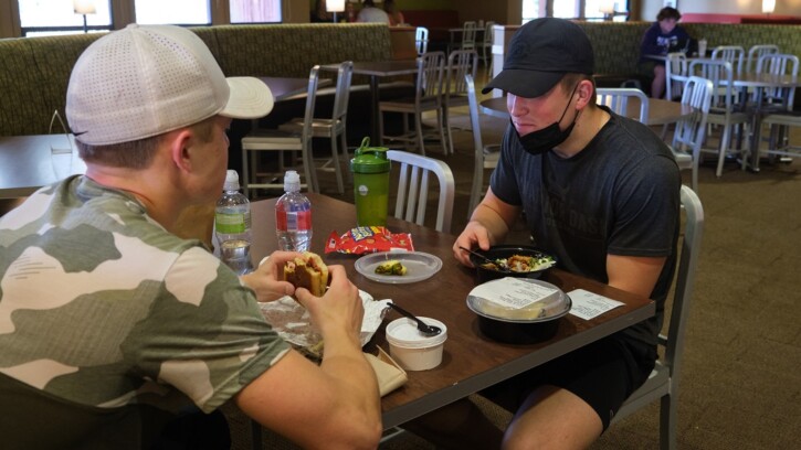 Two students, both wearing baseball caps, eat lunch in the PLU Commons