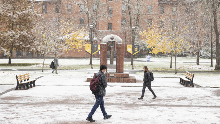 Students wearing backpacks walk across a snowy Red Square in the center of PLU's campus