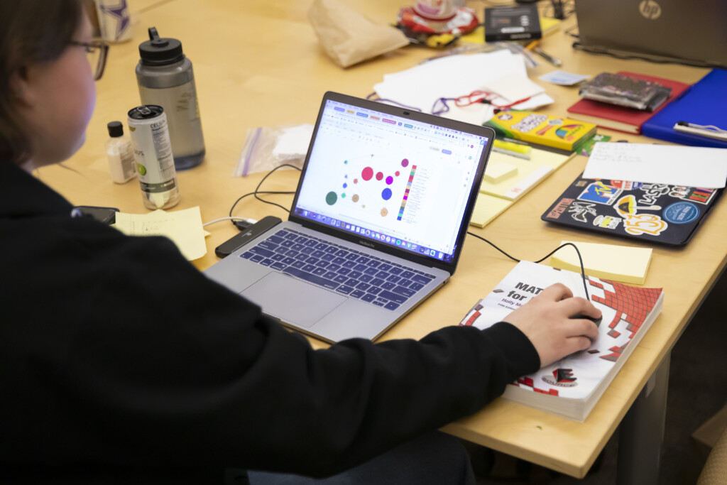 The camera is focused on a laptop screen. The screen shows a math modeling problem.