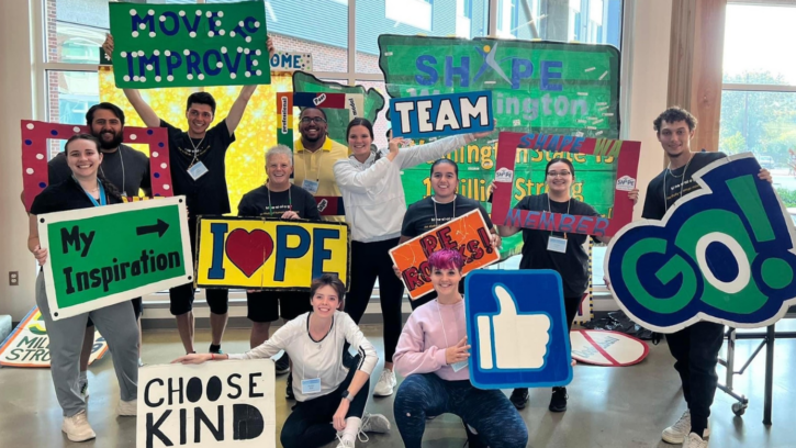 Kinesiology students smile into the camera while holding a bunch of signs with different inspirational messages.