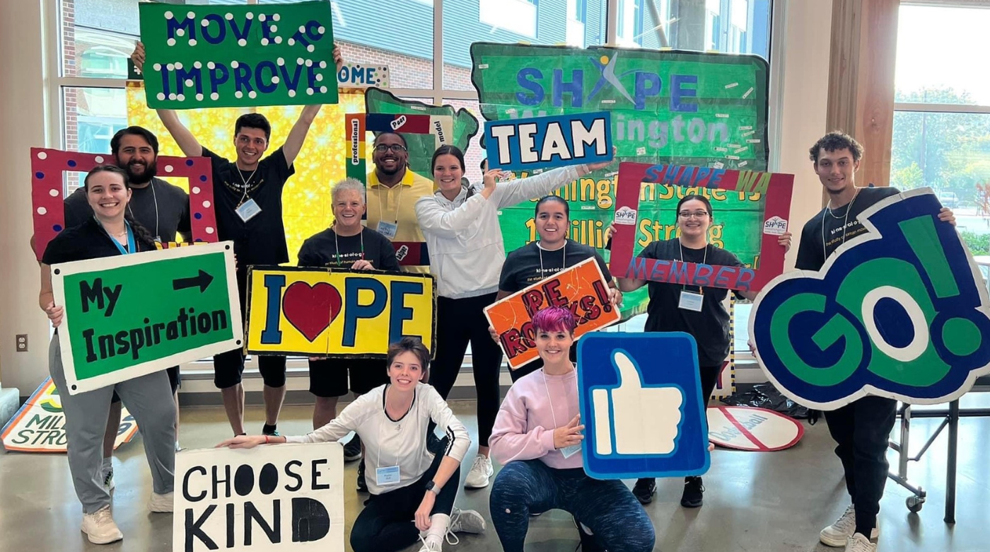 Kinesiology students smile into the camera while holding a bunch of signs with different inspirational messages.