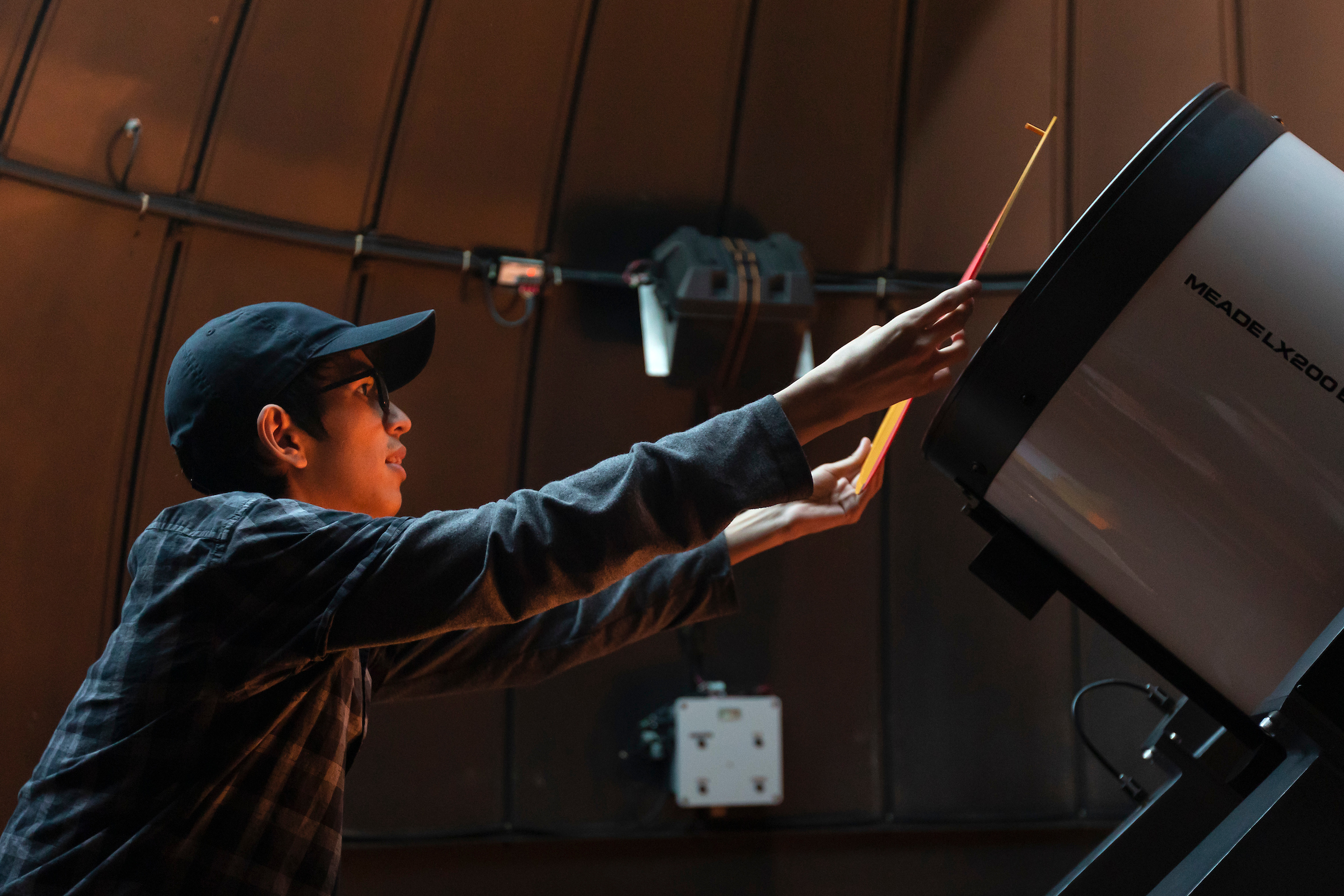 A student puts a orange mask over a telescope.