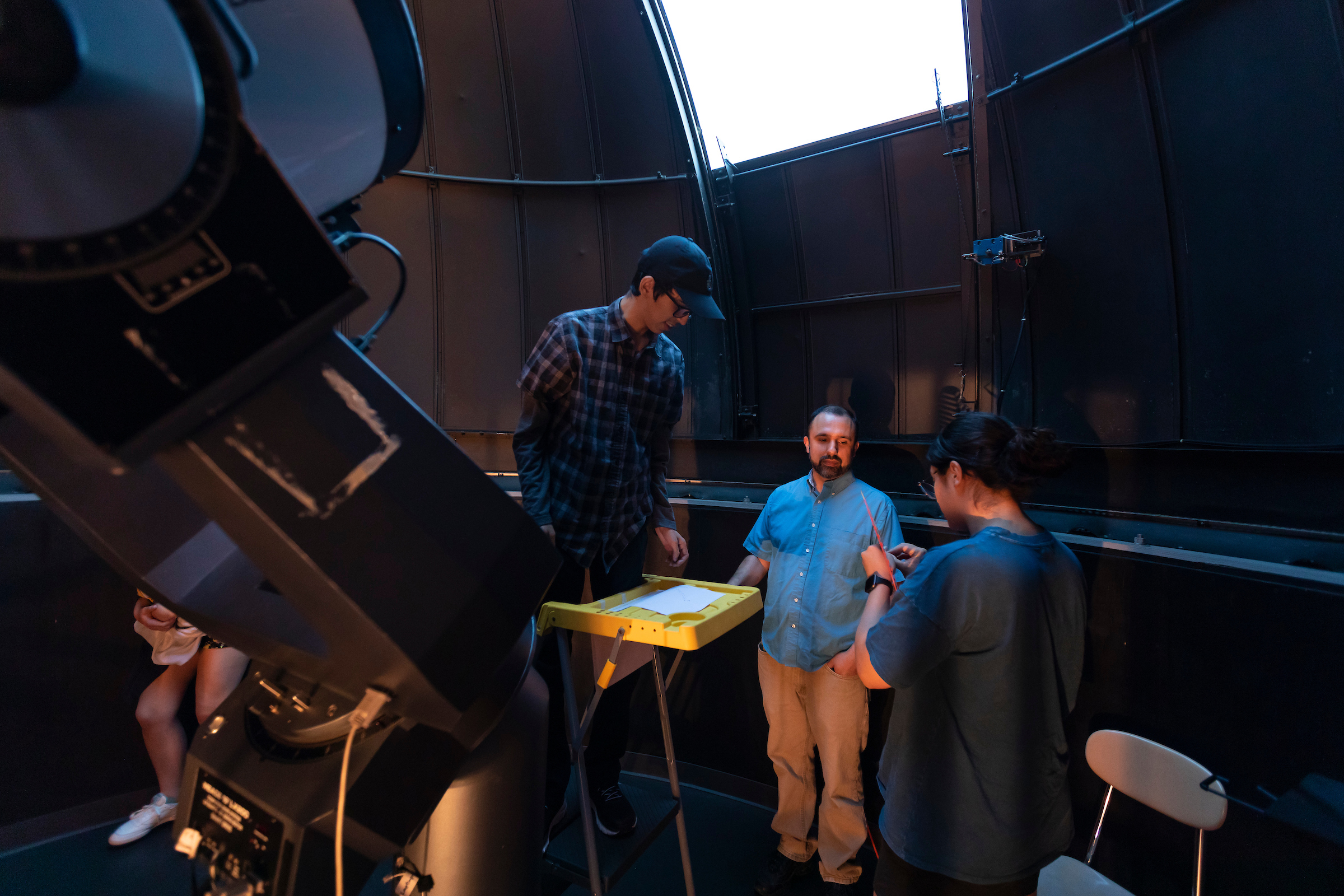 Three people stand under a large telescope.