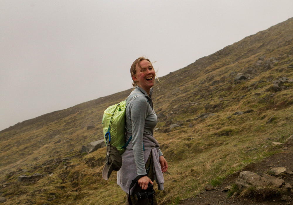 Student smiles into the camera as they walk up a grassy mountain in Iceland.