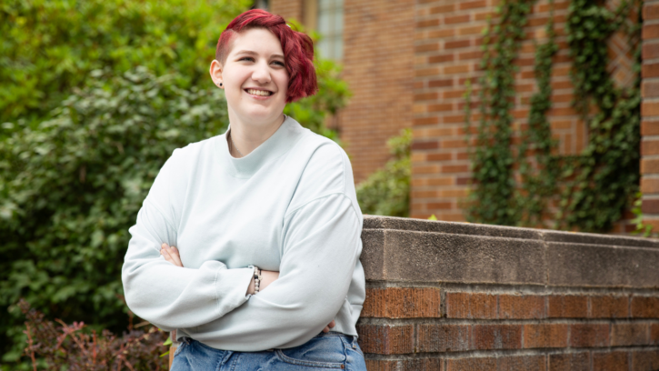 Student wearing a white sweatshirt looks into the distance with arms folder and short red hair.