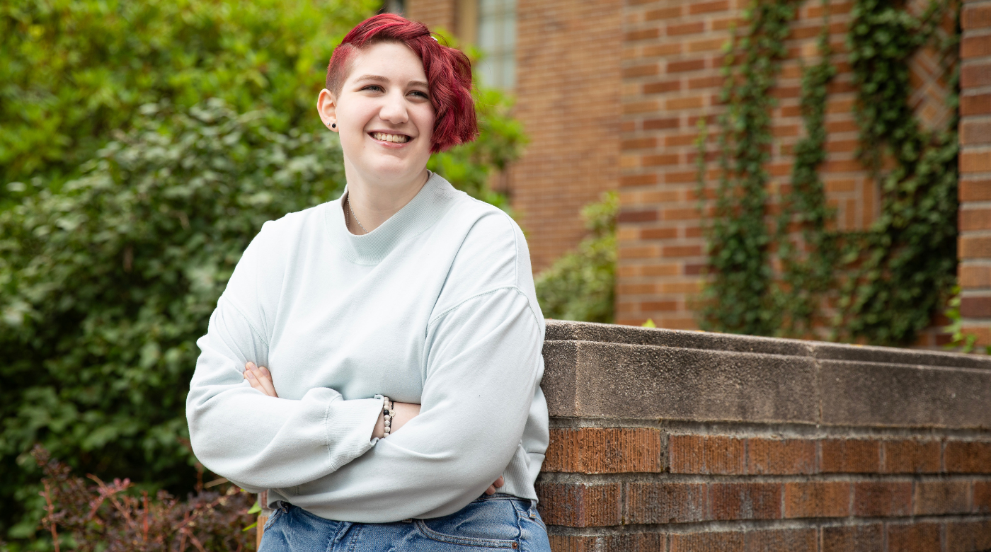 Student wearing a white sweatshirt looks into the distance with arms folder and short red hair.