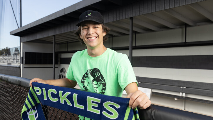 Student smiles into the camera wearing a Portland Pickles shirt and holding a scarf that reads pickles.