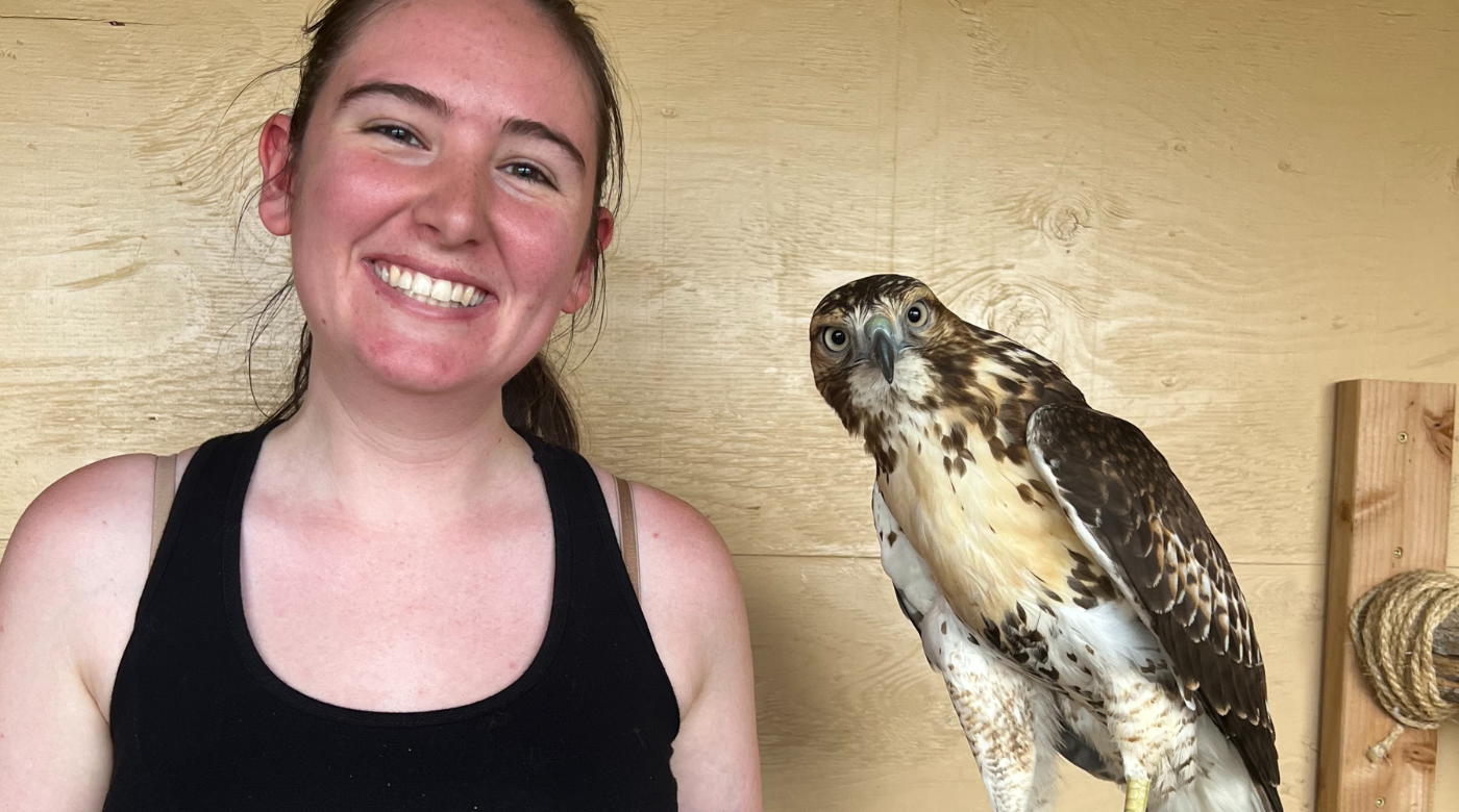 Student holds a hawk and smiles into the camera.