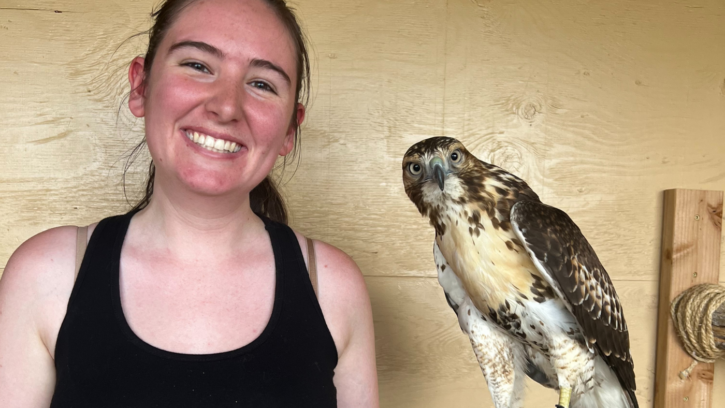 Student holds a hawk and smiles into the camera.