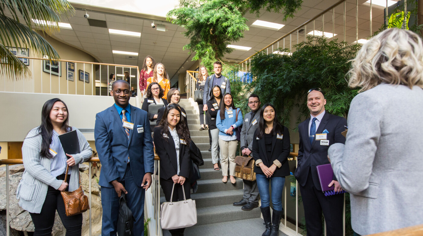 PLU students stand on the stairs at Alaska Air and listen to a presenter. The presenter's back is to the camera.