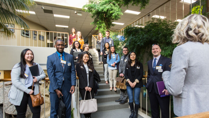 PLU students stand on the stairs at Alaska Air and listen to a presenter. The presenter's back is to the camera.