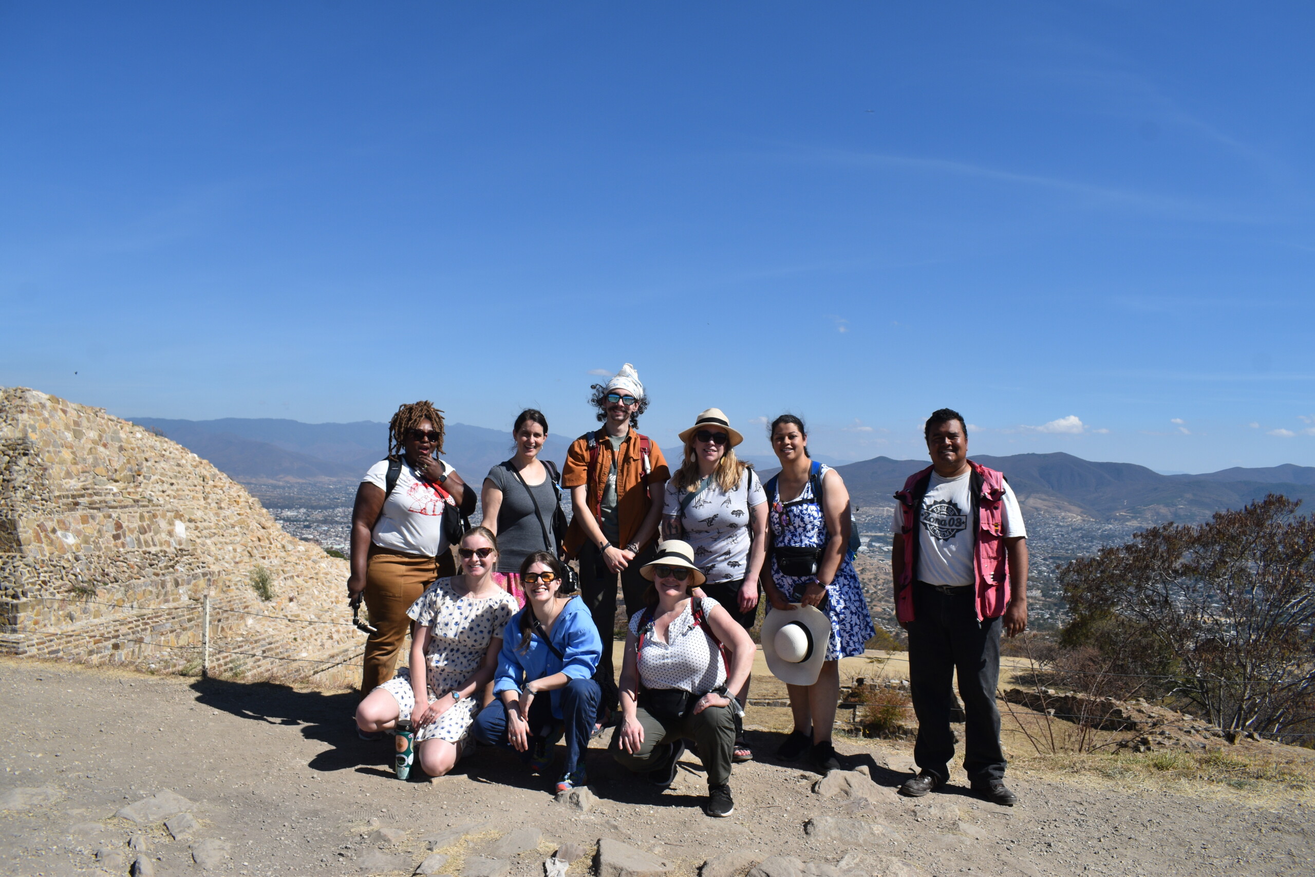 Students studying in Oaxaca, Mexico stand as a group with on a mountain with the landscape in the background and smile into the camera.