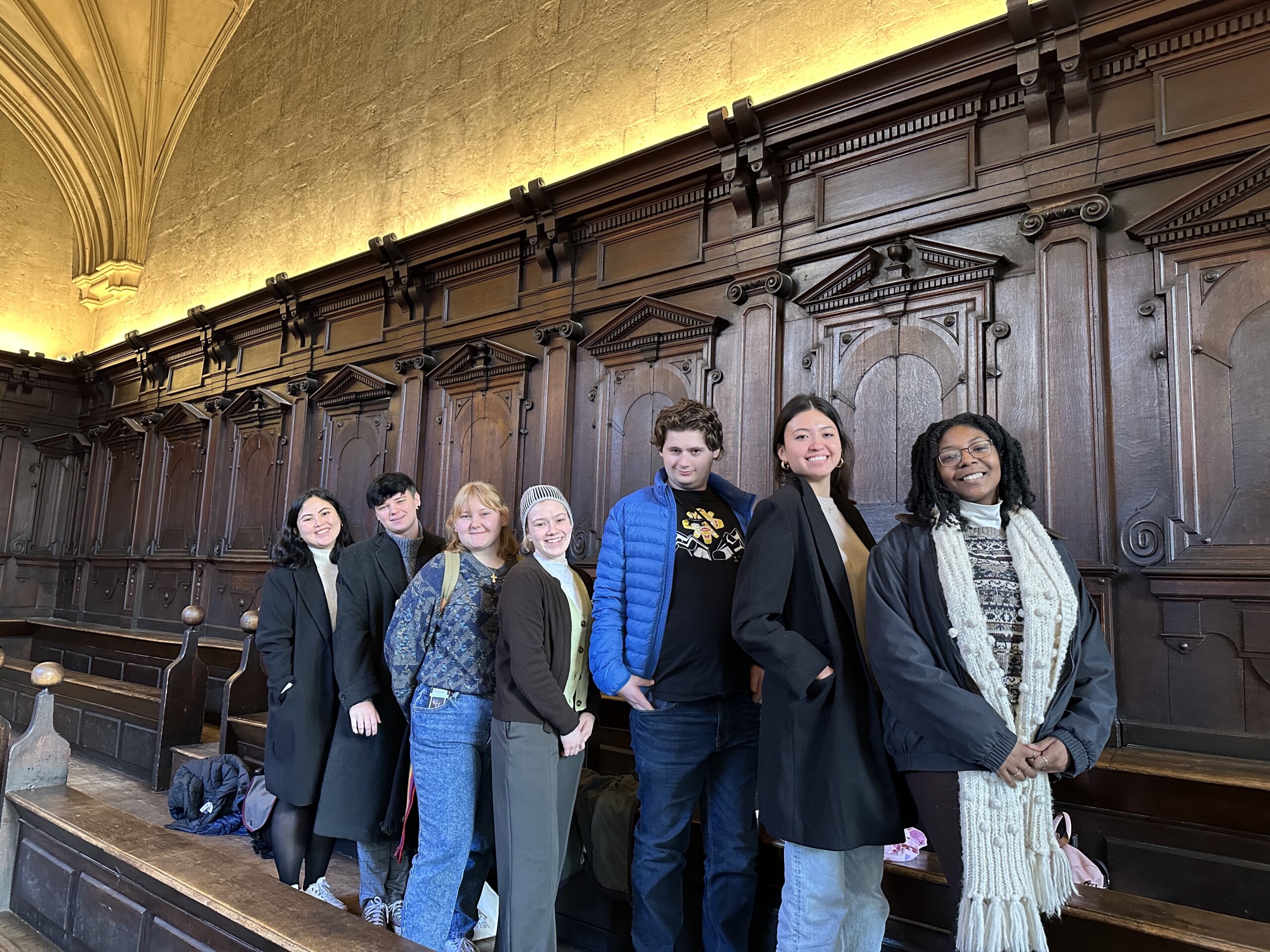 Seven people standing in a line at the Bodleian look into the camera and smile.