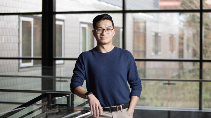 Student looks into the camera wearing a dark blue shirt and leans on a stair rail.