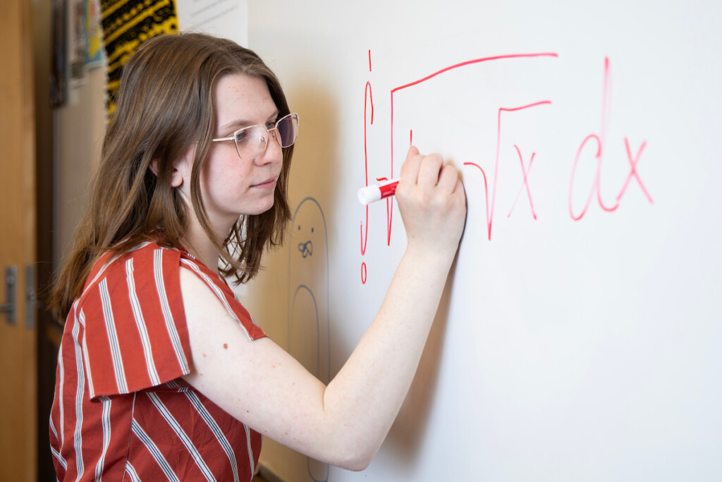 Student writes a math formula on a white board.