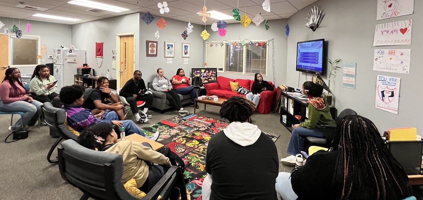 About a dozen students in PLU's Black Student Union sit in a circle in chairs and couches in PLU's Diversity Center during a meeting. Posters and framed artwork are on the walls, and colorful paper snowflakes hang from the ceiling.
