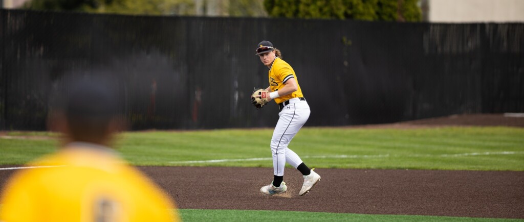 Blog - Carson Burke 02 PLU baseball player Carson Burke in a yellow jersey and white pants, is on the field and ready to throw a ball during a game.
